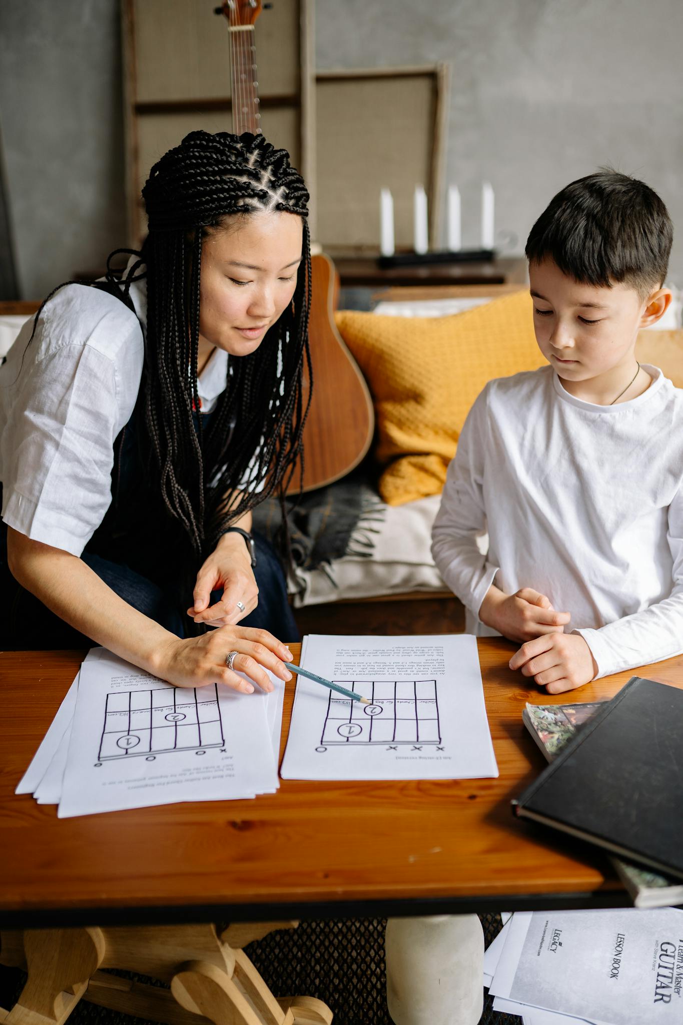 An adult teaching a child to read music notes on a sheet indoors.